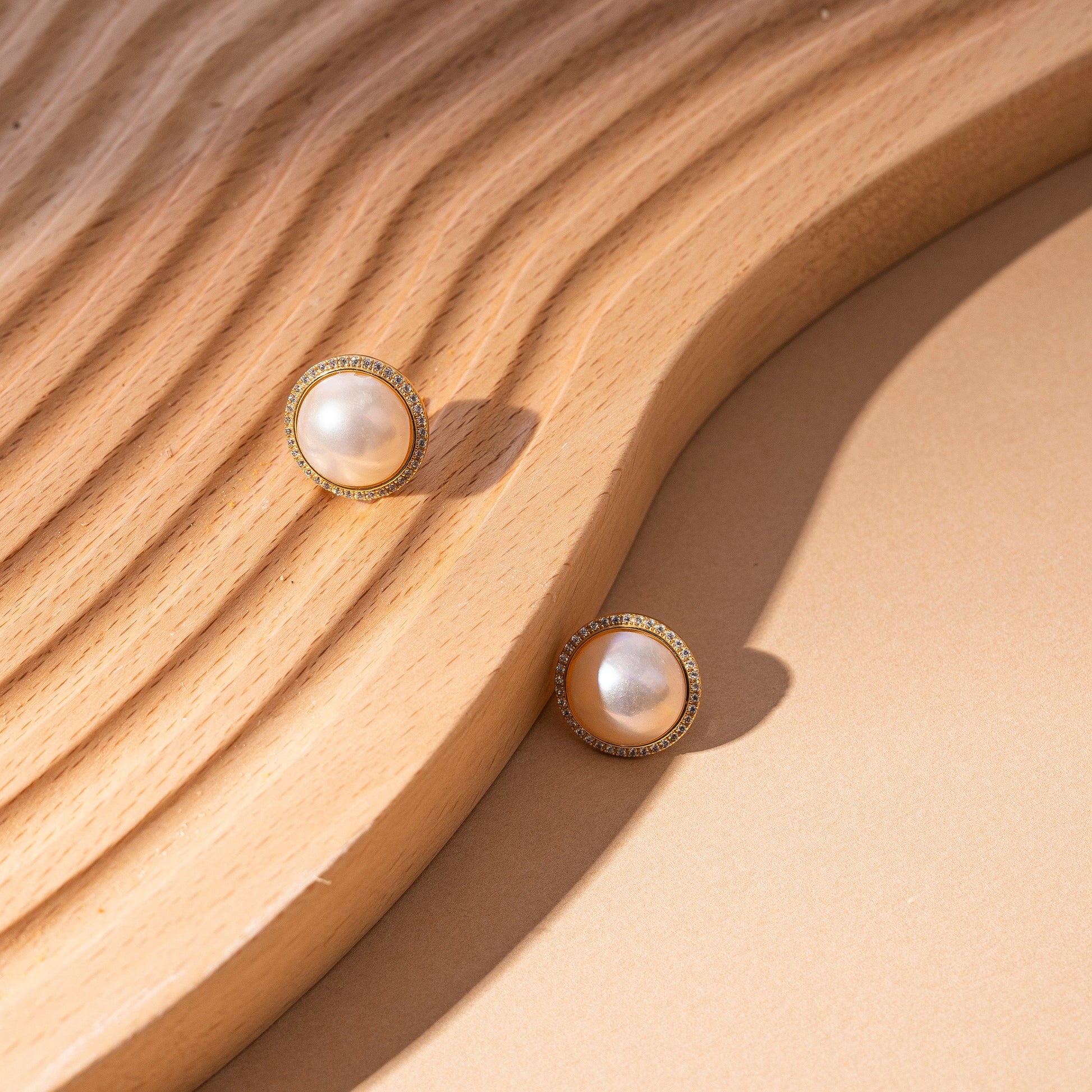 STELLA MARGARITA mabe pearl diamond rim earrings displayed on textured wooden surface