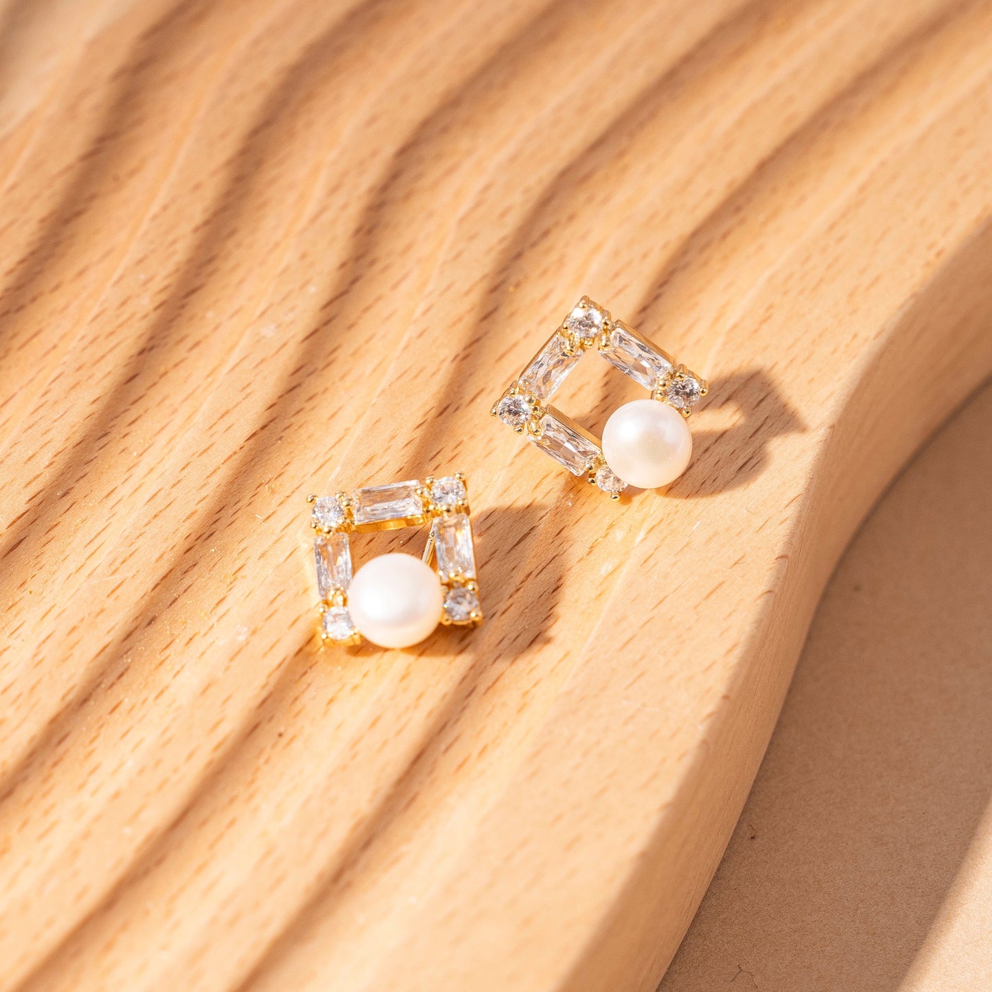 STELLA MARGARITA square pearl stud earrings with gold and crystal accents on wooden surface