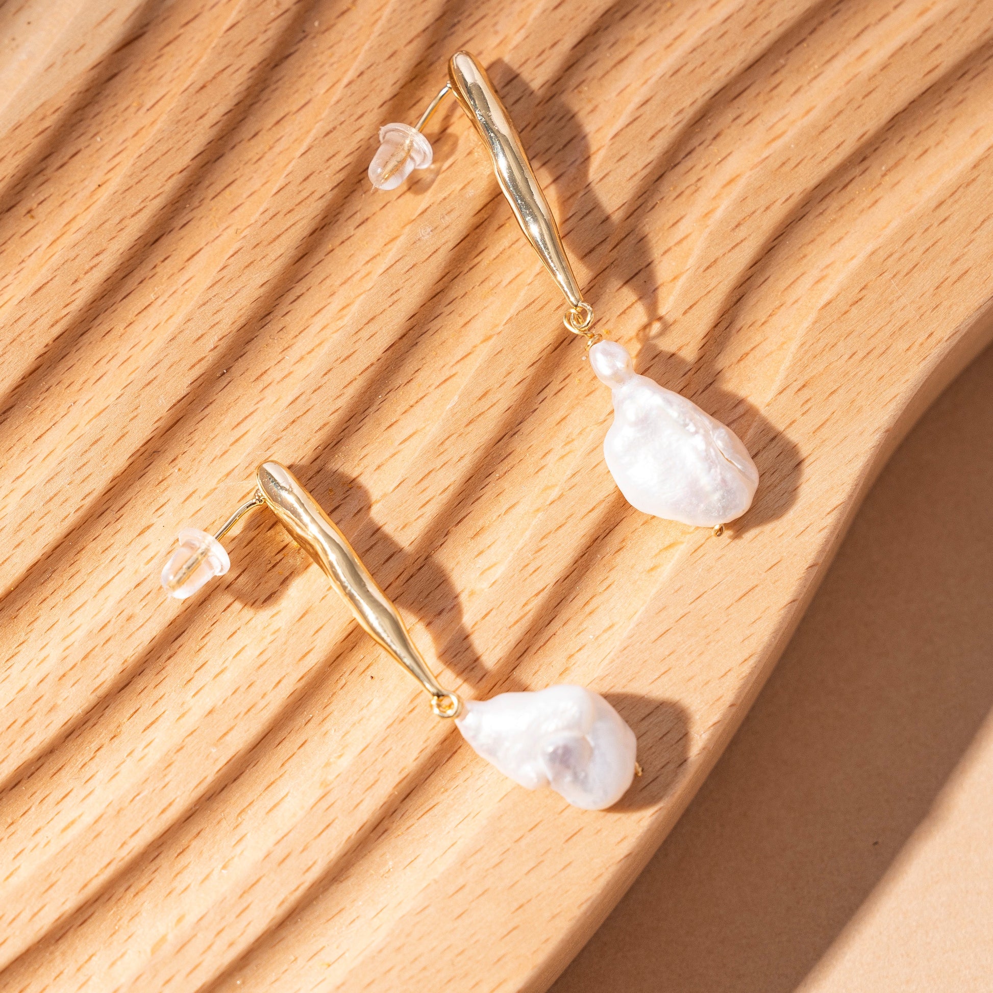 STELLA MARGARITA baroque pearl drop earrings with gold irregular shaped hooks on wooden background
