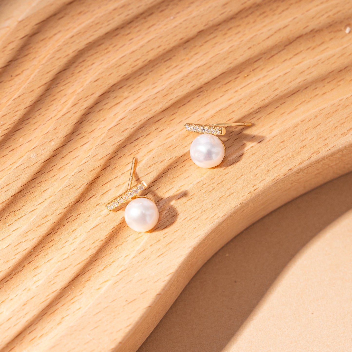 STELLA MARGARITA balance beam pearl stud earrings with gold and crystal detailing on wooden surface