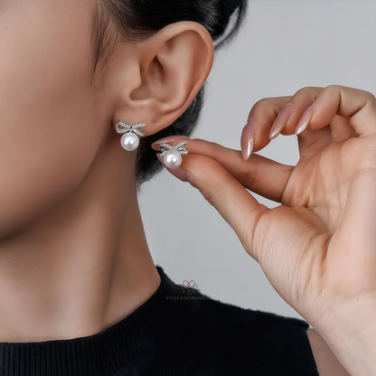 Silver ribbon pearl stud earrings worn on ear and held by hand by Stella Margarita